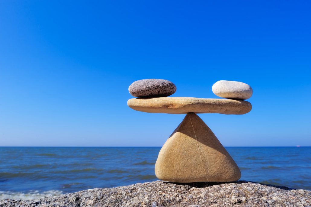 three rocks balancing on top of one bottom rock in front of a blue sky and blue ocean