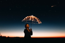 Woman under lit up umbrella stars in the sky