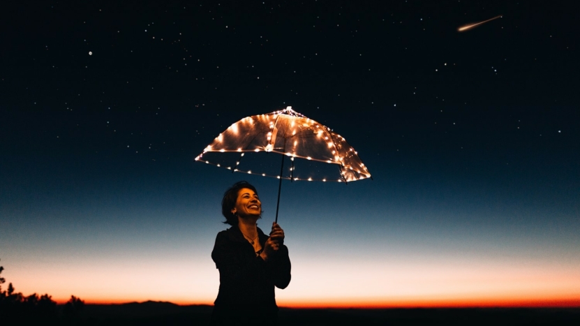 Woman under lit up umbrella stars in the sky