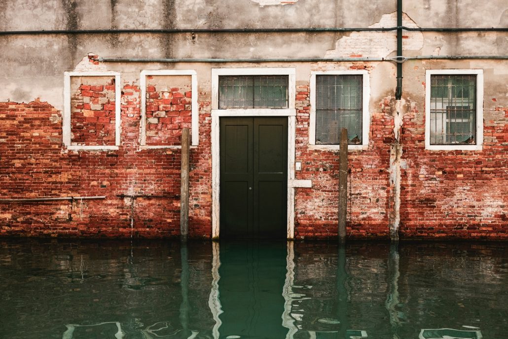 Photo of a brick house under water due to a flood. Every lender is required to screen every property for flood zone status.
