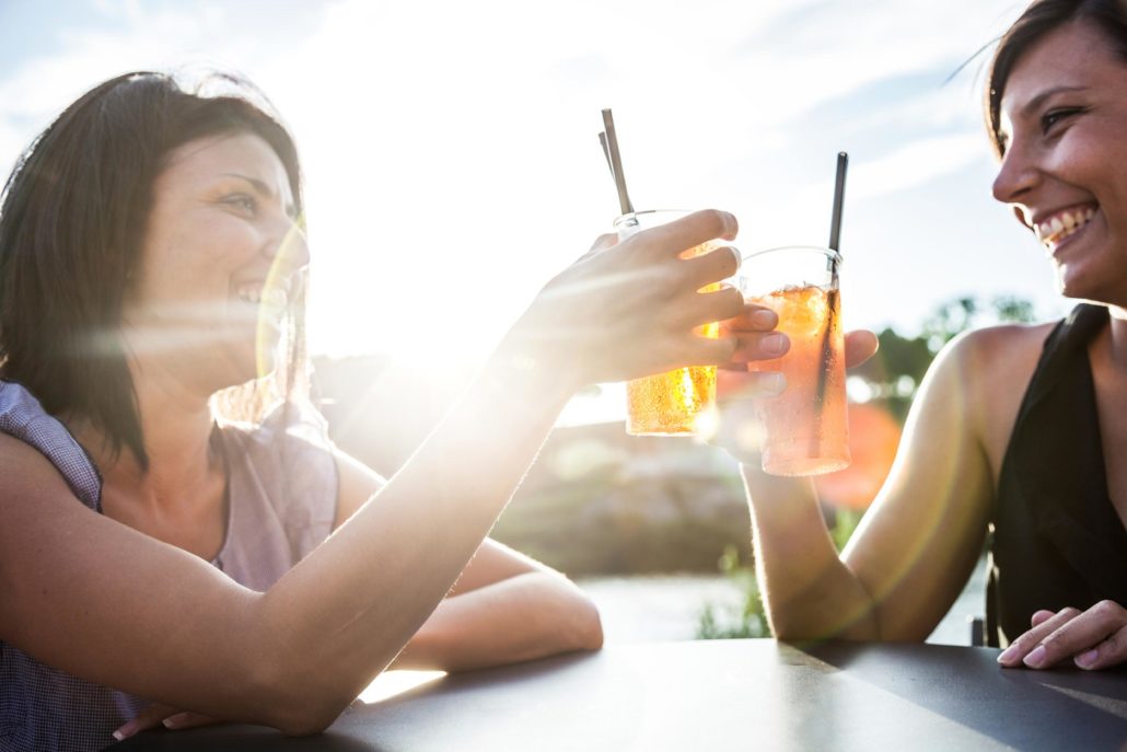 two women sitting outside in the sun raise their vodka drinks to one another while discussing their mortgage lenders