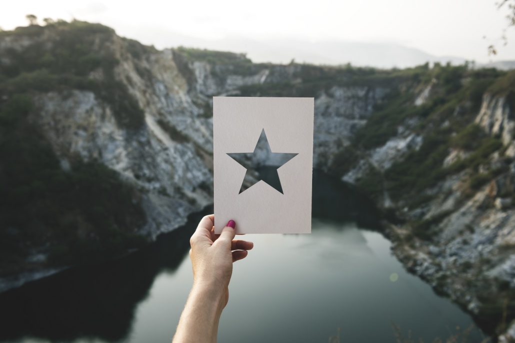 Photo of a star cut out of paper held up against a canyon and lake 