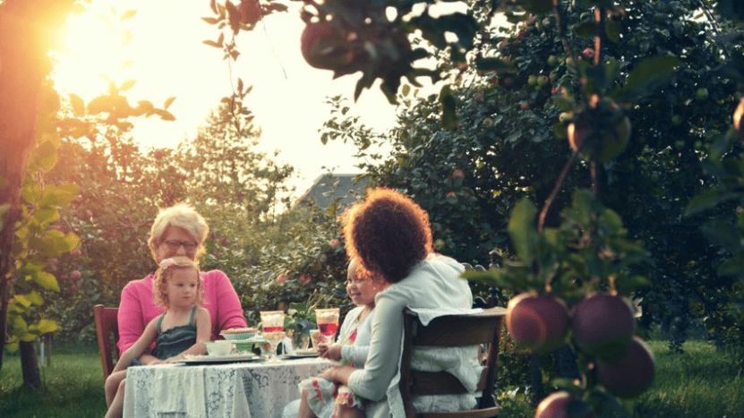 Moms and daughters sitting at table outdoors with food