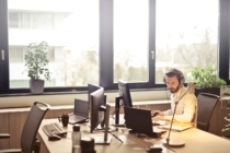 business man sitting at an office desk wearing headphones while looking at a computer monitor reading about the current liquidity crisis