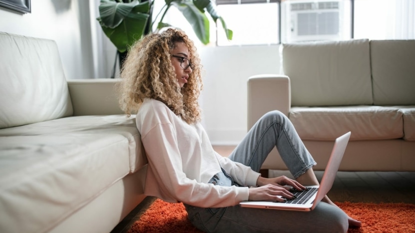 young woman with curly hair sitting on living room floor looking at mortgage rates on a laptop