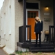 Blonde woman standing in front of her house with an orange door after closing on her refinance.