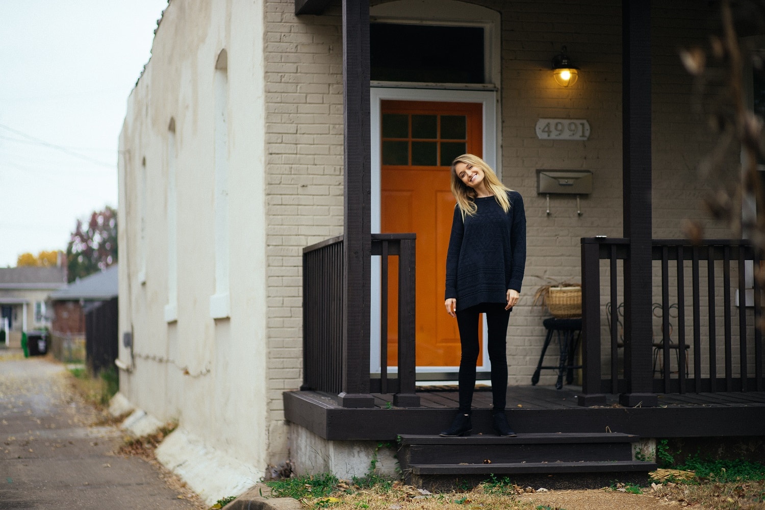 Blonde woman standing in front of her house with an orange door after closing on her refinance.