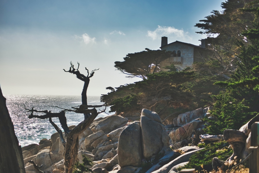 home on a sea side cliff with trees, brush, and rocks in Carmel California where many are moving to this suburbia to avoid higher rent and longer commutes and safer overall living