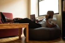 man seated in a bean bag chair with his feet resting on a coffee table looks at the laptop in his lap to review his loan contingency due to COVID-19