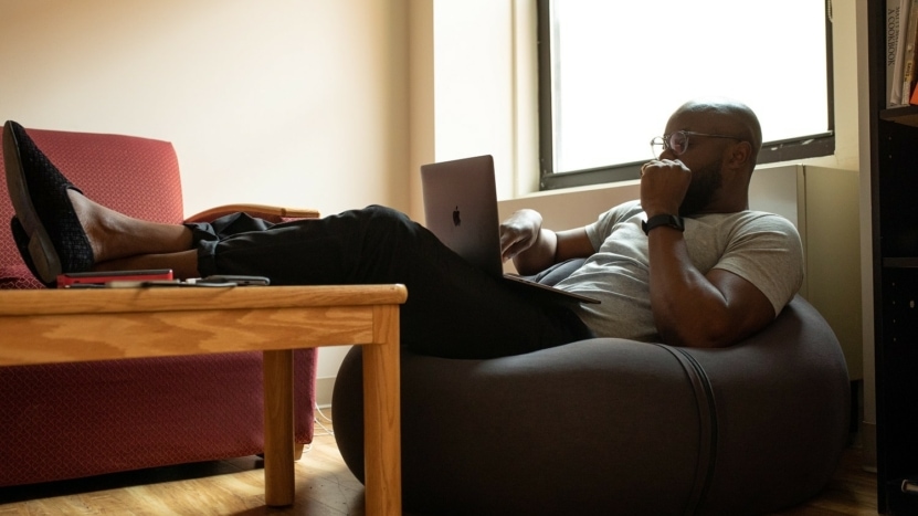 man seated in a bean bag chair with his feet resting on a coffee table looks at the laptop in his lap to review his loan contingency due to COVID-19