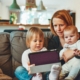 Woman sits at home on the couch with her two young children and looks up her home value using Homebot on her tablet.
