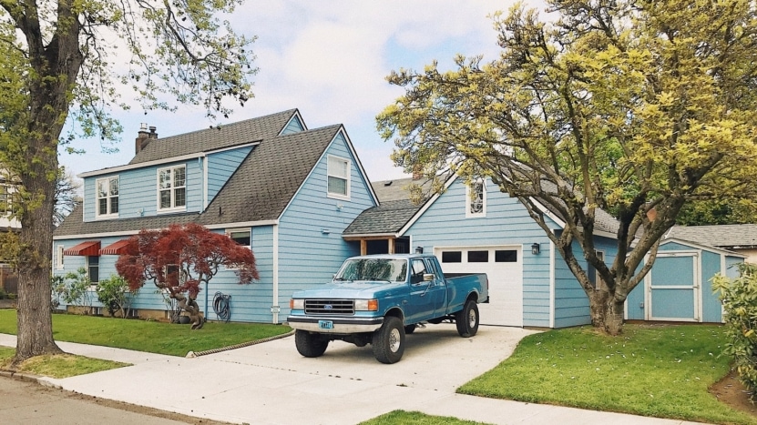 a blue house in the suburbs with a blue tuck parked inthe driveway and trees on either side of the home with a lawn