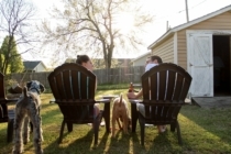 a couple sit in their backyard with dinner and drinks as they enjoy dinner with their two dogs