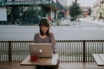 A young woman sits outside of a coffee shop on her laptop working on a rapid re-score