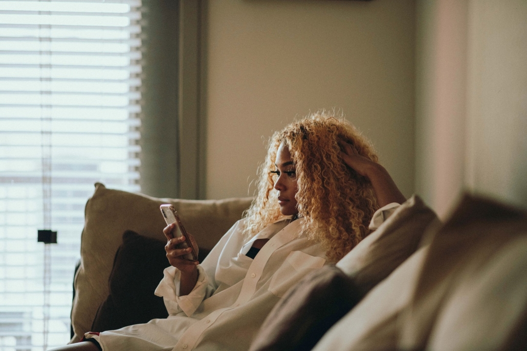 A woman sits on the couch and looks up the status of her credit rapid re-score on her phone.