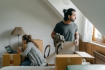 Man packing clothes in a box while women uses laptop