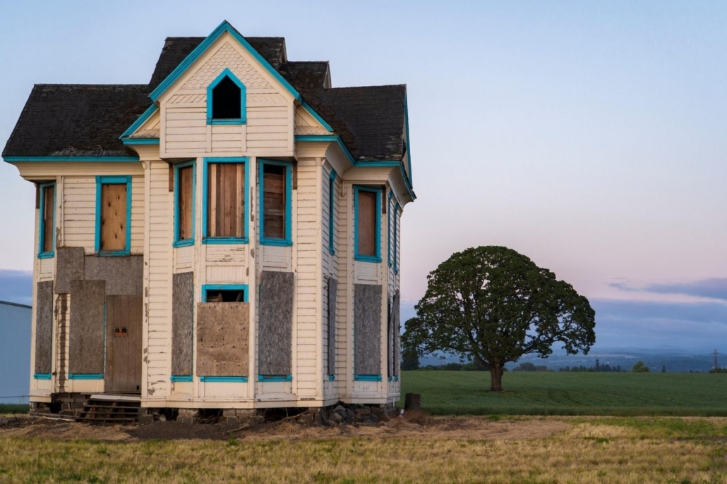 an abandoned two story home located in one of California's fire areas sit in front of a green field with a city skyline in the very far background