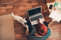 a woman interested in a refinance sit on the floor with her laptop and dog while reading about the new 50 point refinance fee by Fannie Mae and Freddie Mac