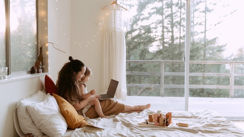 A mother and daughter sit together on a bed looking up homes on a laptop. Housing demand is surging right now with limited inventory and many millennial buyers.