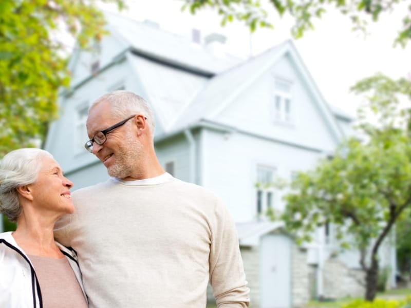 Elderly couple smile at each other in front of home