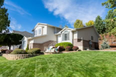facade of home with manicured lawn, and backdrop of trees and blue sky