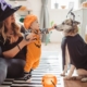 Mom holds up a a baby dressed as a pumpkin to pet dog dressed as a vampire the day before halloween