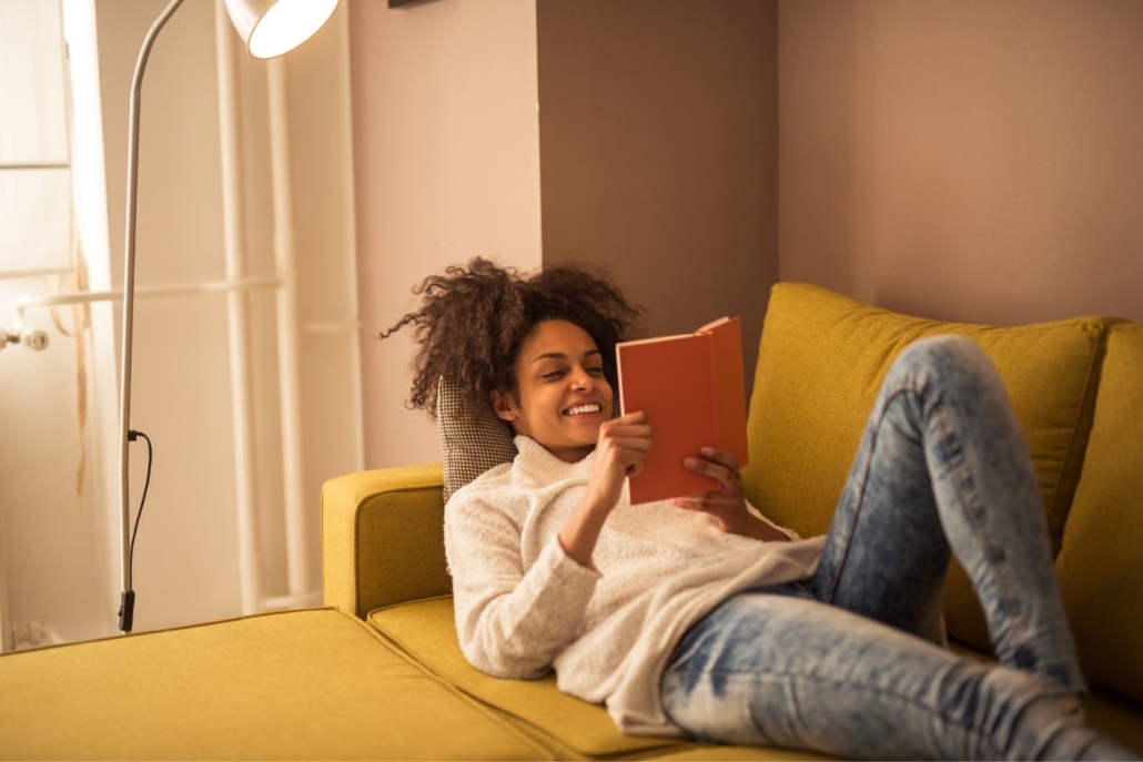 a young black woman lounges on a yellow couch reading a book on coaching