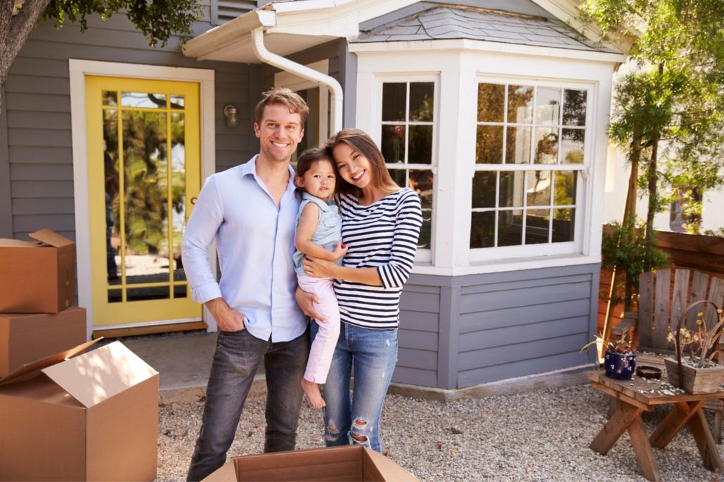 Couple with a baby standing in front of home with moving boxes