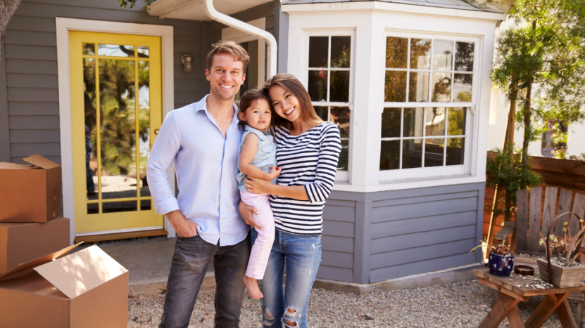 Couple with a baby standing in front of home with moving boxes