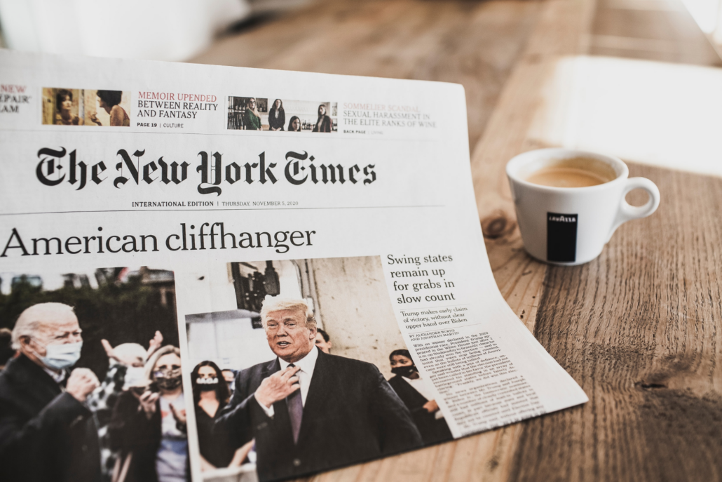 New York Times newspaper with president elect Joe Biden and former president Trump held in front of coffee cup on a table