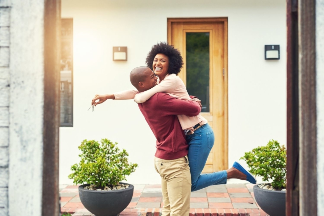 a man and woman hug, with the man lifting the woman, holding house keys, off the ground in celebration of buying their new home using JVM Lending’s fast 14 day close