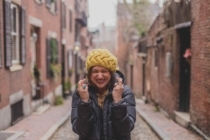 A woman in a yellow hat and a black coat crosses her fingers for luck and remains optimistic despite expecting the worst.