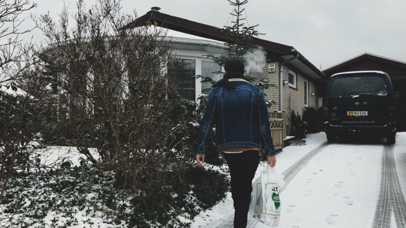 A man walks to his house in the winter carrying groceries. He purchased his home using points and potentially wasted his money.
