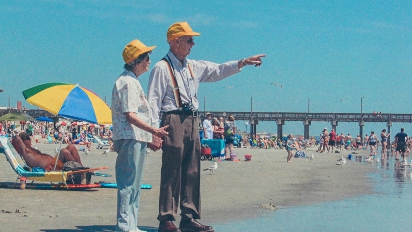 An elderly couple at the beach wear vintage clothes and look out with nostalgia and reminisce about the good old days.
