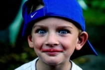 A young boy with a backwards blue Nike hat smiles for the camera with a Kool-Aid smile