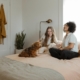 Two women sit together on a bed with their dog after they locked in their refi rate with their lender.