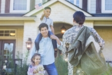 A female military soldier returns home to her family wearing her uniform after being away. Her home was purchased using a VA loan - available to all veterans and active service members.