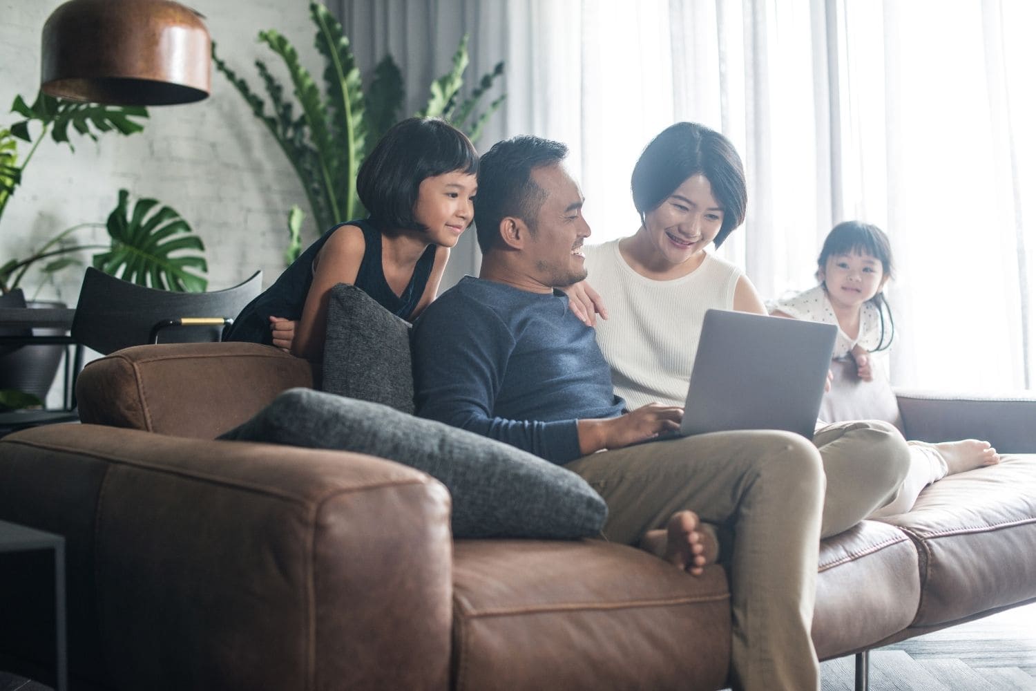 family of four sit on the couch looking at a laptop to read about how DACA status recipients can indeed obtain both FHA and conforming mortgage loans