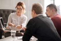 Woman holding laptop explains something to two men