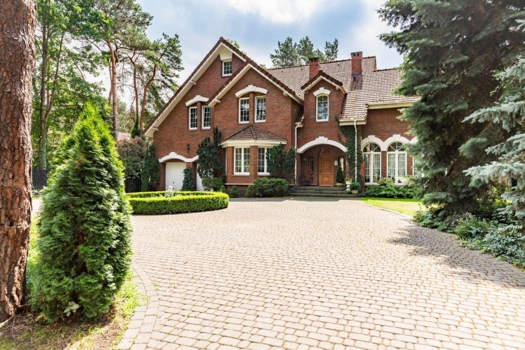 expensive two story red brick house with brick driveway surrounded by trees