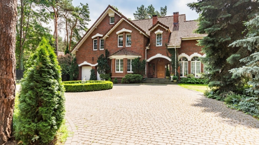 Red brick house with brick driveway surrounded by trees
