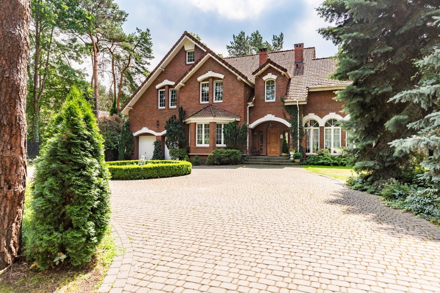 Red brick house with brick driveway surrounded by trees