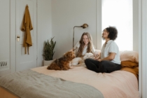 Two young women sit on the bed in their new home that they just got their offer accepted on after using these 8 tips.