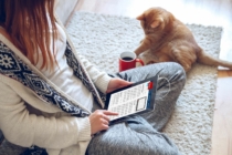 woman sits on floor reading the news on an iPad about mortgage rates climb. An orange cat sits on the floor next to her.