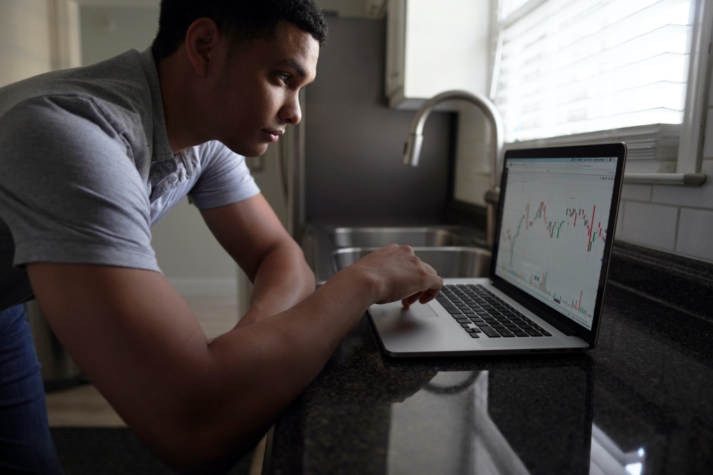 A young man looks at his laptop computer in the kitchen as he considers how to best diversify his assets to protect against inflation and deflation.
