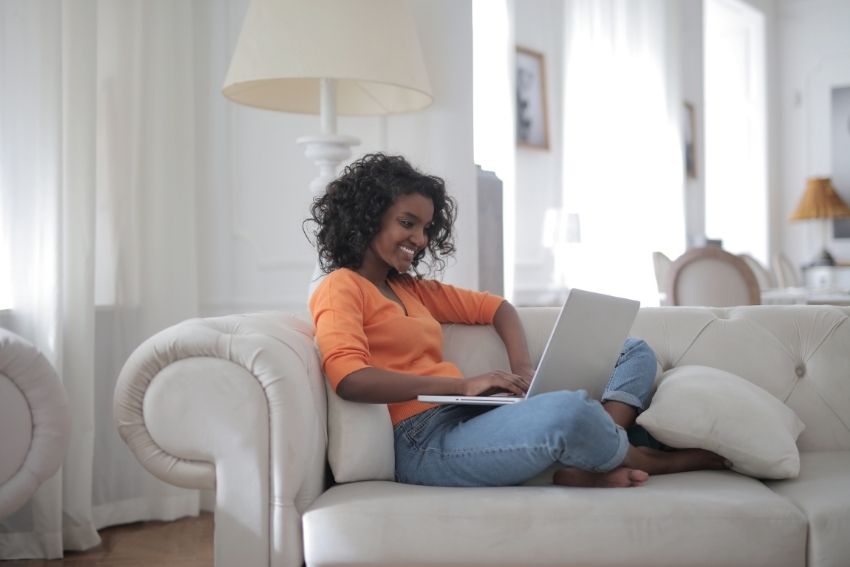 woman sitting on white couch with laptop reads about re-amortizing her mortgage