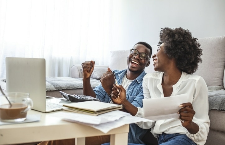 Happy black couple reading PMI documentation at home on the couch, checking agreement details together.