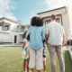 Family in their backyard together looking at their property or luxury real estate. Embrace, mortgage and parents with their children on grass at their home.