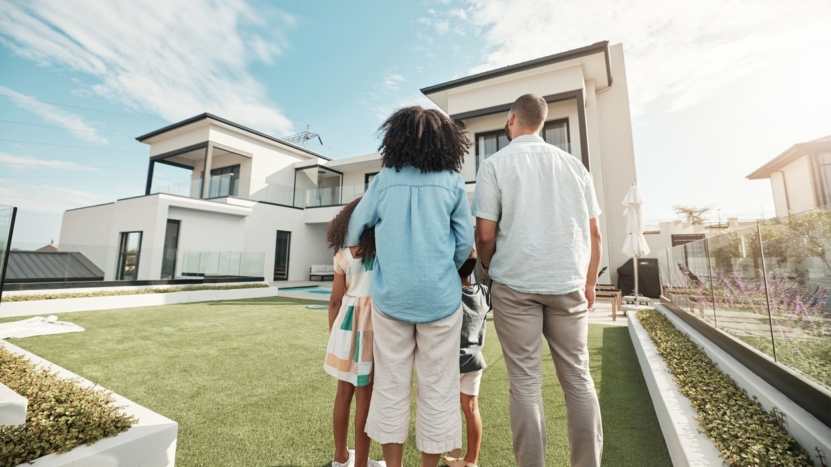 Family in their backyard together looking at their property or luxury real estate. Embrace, mortgage and parents with their children on grass at their home.