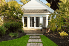 A cute white house with a lush green back yard lined with pavers.